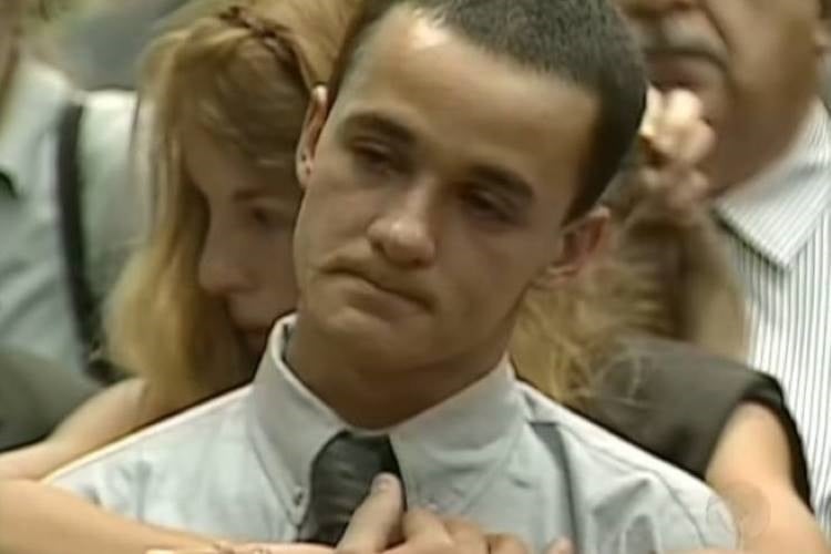 Daniel Cravinhos com semblante triste usando uma camisa social e gravata, sendo abraçado por Suzane. 