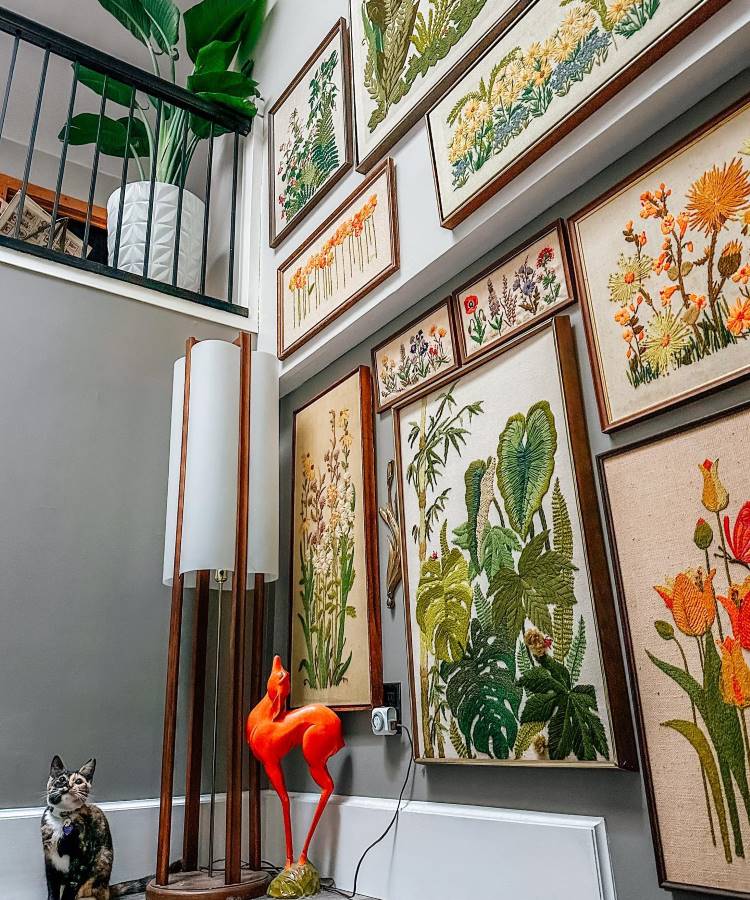 Quadros bordados com desenhos de plantas em parede, com outros objetos como luminária, gato e veado na decoração da casa