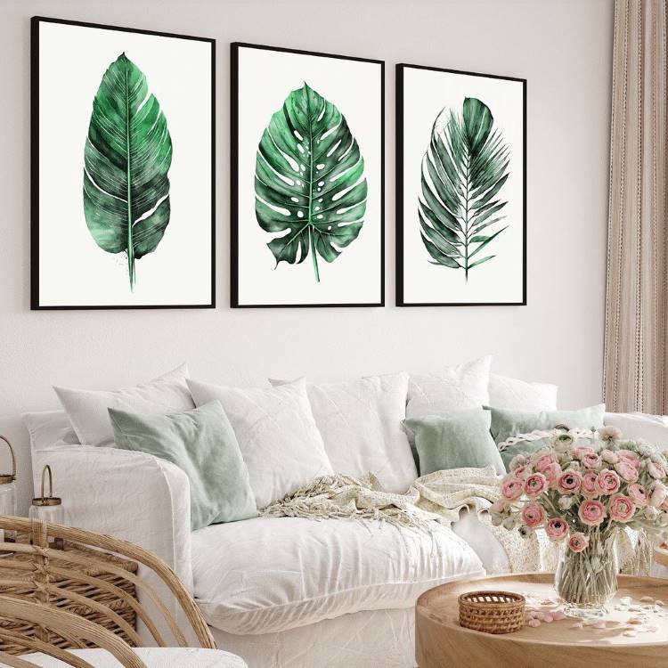 Sala de estar com sofá branco, almofadas, arranjo de flores na mesa de centro e quadros de folhas na parede