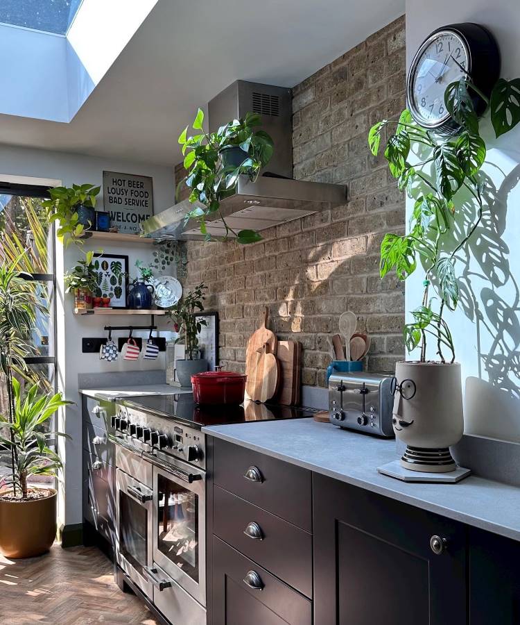 Cozinha com móveis pretos e parede de tijolinhos decorada com plantas e quadros