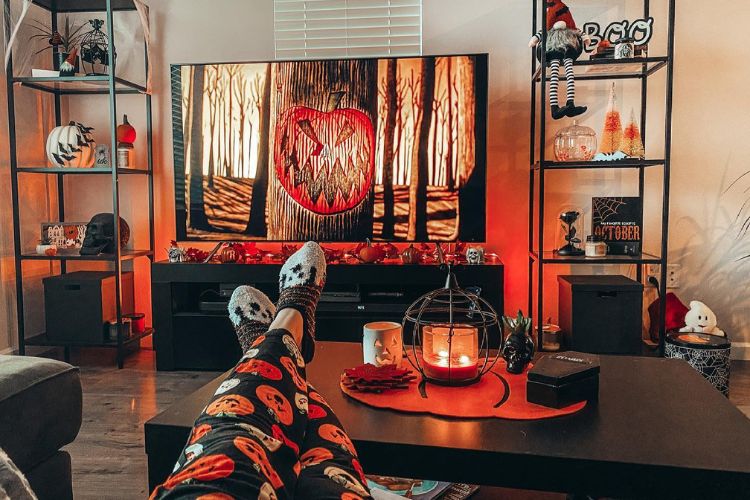Decoração de Halloween com led laranja, abóbora na TV, centro de mesa com velas e itens de Dia das Bruxas nas estantes