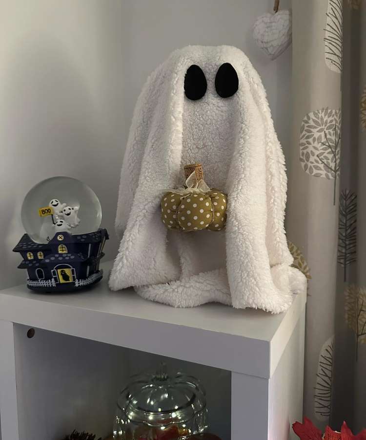 Fantasma feito com cobertor branco segurando abóbora em móvel de decoração