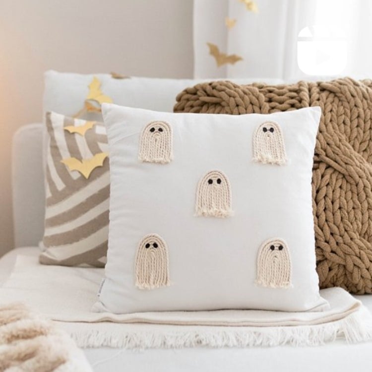 Almofada com decoração de fantasmas feitos de barbante em sofá com outras almofadas