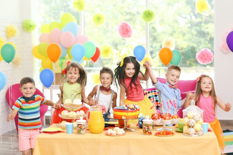 Foto de crianças sorrindo atrás de mesa com doces, decorada em amarelo e com bexigas coloridas