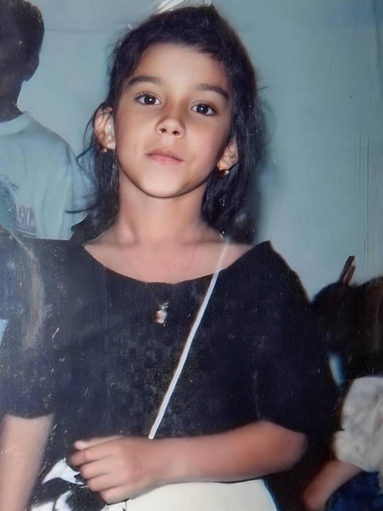 Foto de Jenny Miranda criança vestindo uma blusa preta. Ela estava de cabelo semi preso e com uma bolsa de alça transversal branca. 