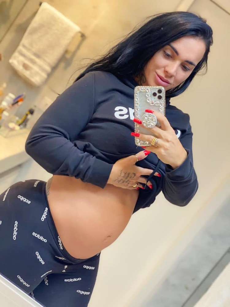 A peoa grávida em 2020, foto no espelho em banheiro, ela usando roupa preta da adidas e mostrando a barriga