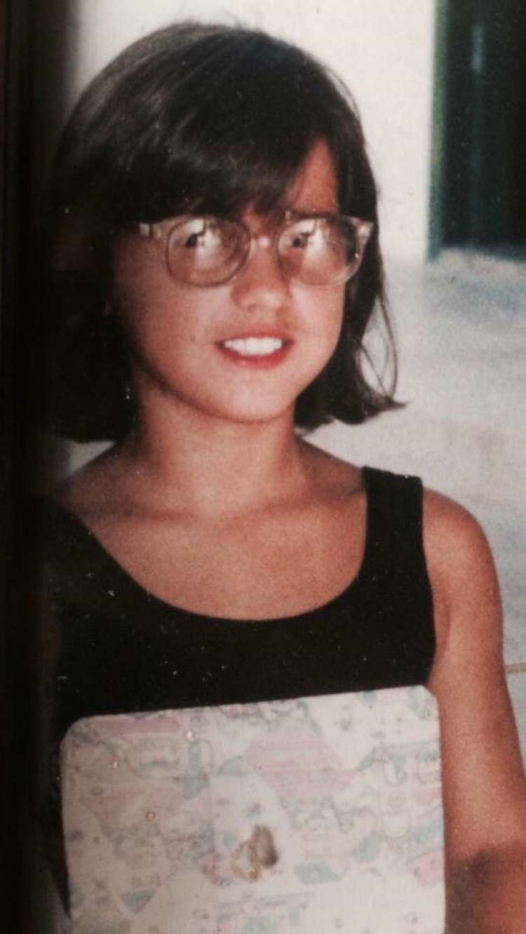 Kamila Simioni criança, usando óculos e regata preta, de cabelo curto com franja