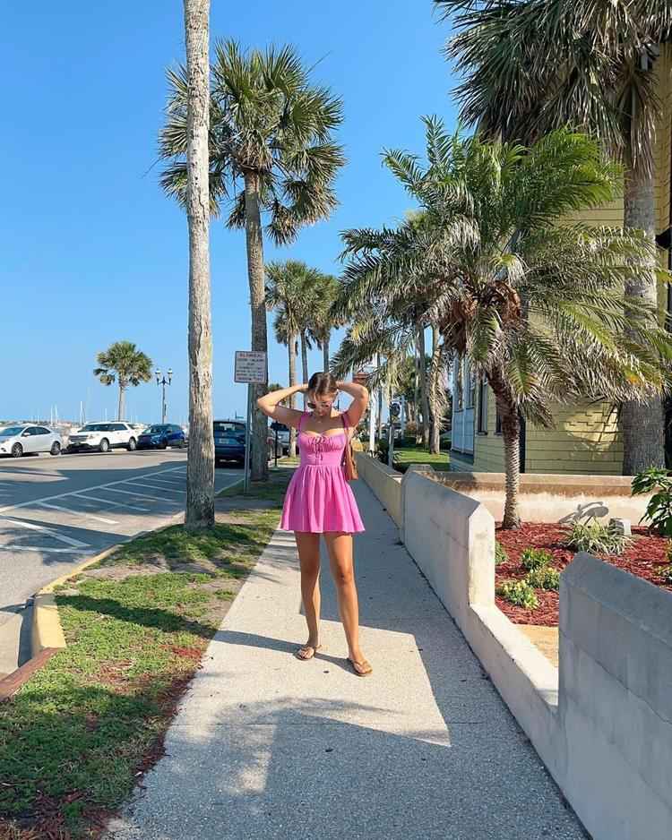 mulher em rua de praia com vestido curto rosa de alça