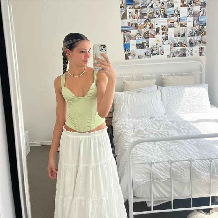 mulher em quarto tirando foto no espelho com corset verde e saia longa branca