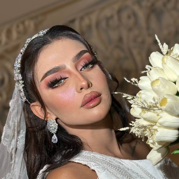 Noiva morena maquiada, usando véu, acessórios de cabelo, joias, vestido branco e segurando buquê de tulipas creme