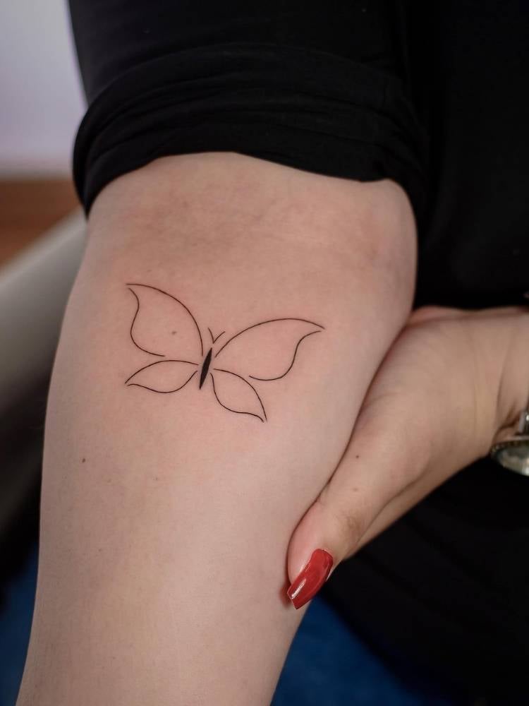 Tatuagem minimalista de borboleta com traços finos em parte interior do antebraço de uma mulher e pele clara.