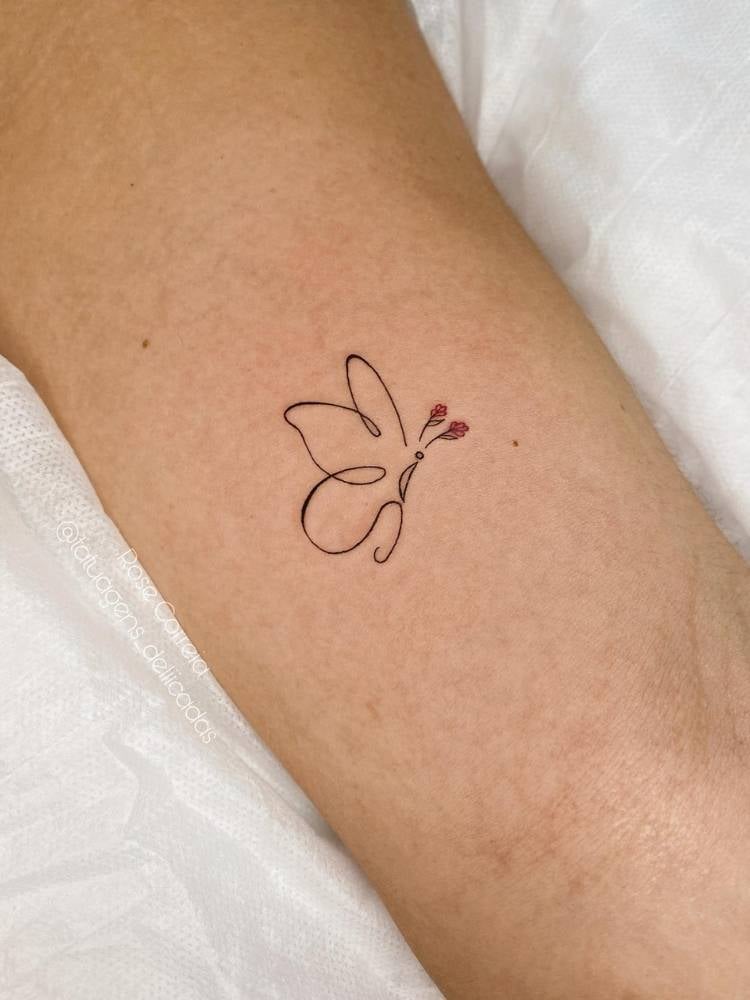 Ttuagem de borboleta em traço fino minimalista, cujas antenas são em formato de rosas. Ela foi feita no interior do braço de uma mulher de pele clara. 