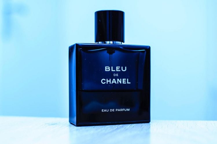 vidro do perfume de verão Bleu de Chanel em cima de superfície branca com fundo azul. O frasco da fragrância é azul marinho