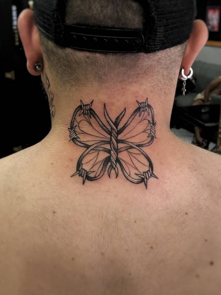 Tatuagem de borboleta com traços grossos e espinhos nas asas. Feita na nuca/costas de um homem de pele clara. 