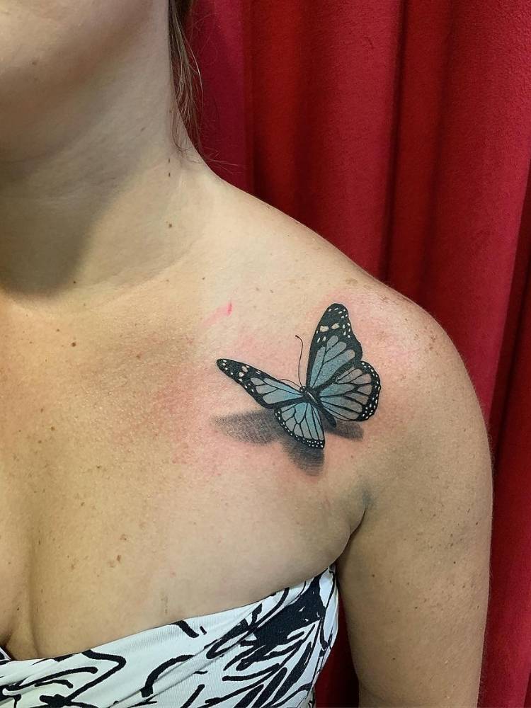 Tattoo de borboleta-azul com sombreamento efeito 3D no ombro de uma mulher de pele clara. 