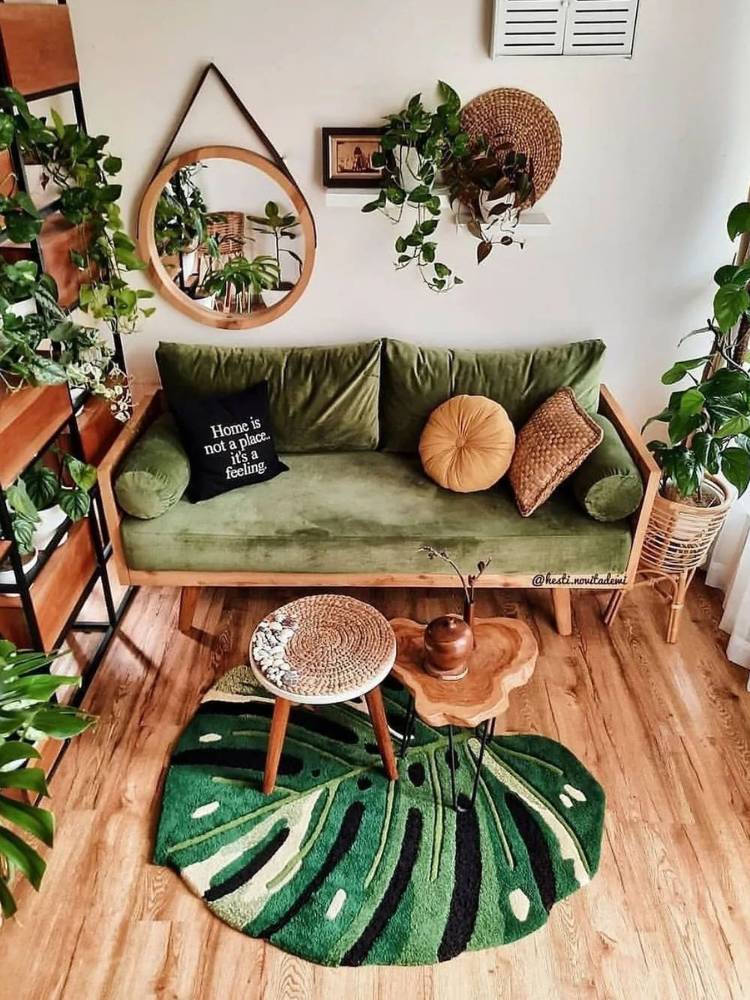 Sala com piso de madeira, sofá verde, paredes brancas, diversas plantas ao redor do cômodo, espelho redondo no canto esquerdo, tapete em formato de Monstera com duas mesinhas de centro em cima. 