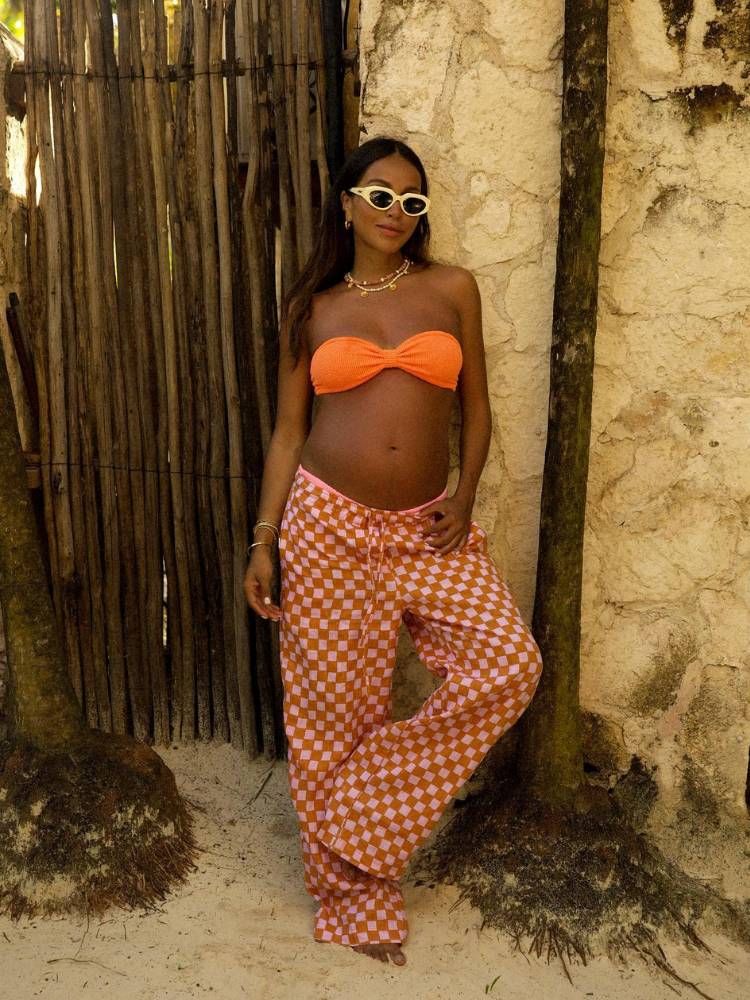 Mulher grávida com top de praia sem alça na cor laranja e calça quadriculada também em laranja. 