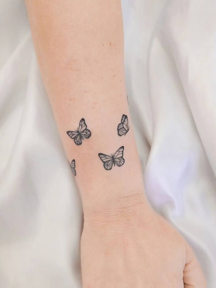 Tatuagem de borboletas pequenas em traço fino no pulso, formando uma espécie de bracelete. Foi feita numa mulher de pele clara. 