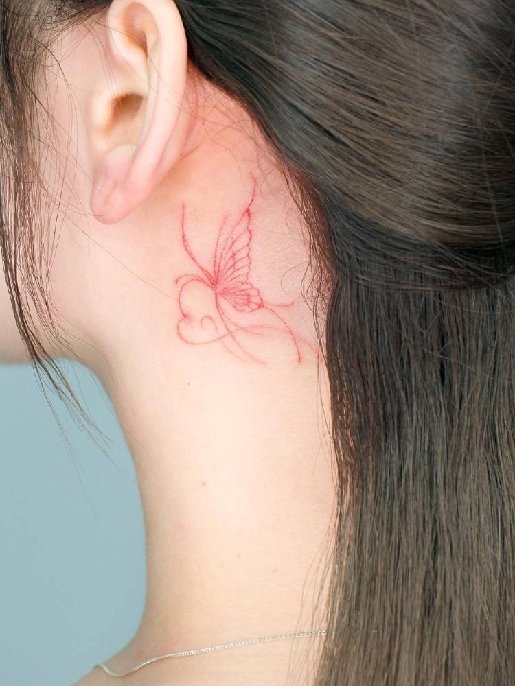 Tatuagem de borboleta em traço fino vermelho na nuca de uma mulher de pele clara e cabelo liso marrom. 