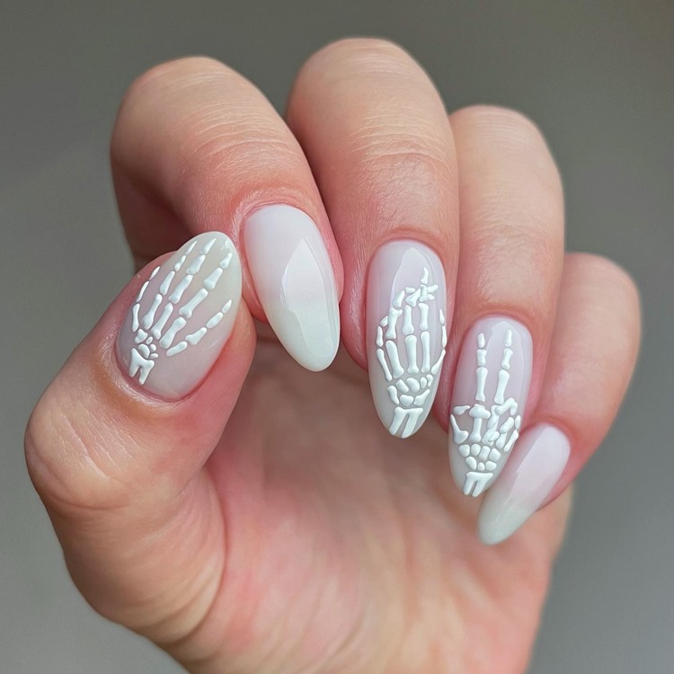 Mão com unhas grandes amendoadas decoradas com mão de esqueleto para o Halloween, nas cores branco transparente e branco puro