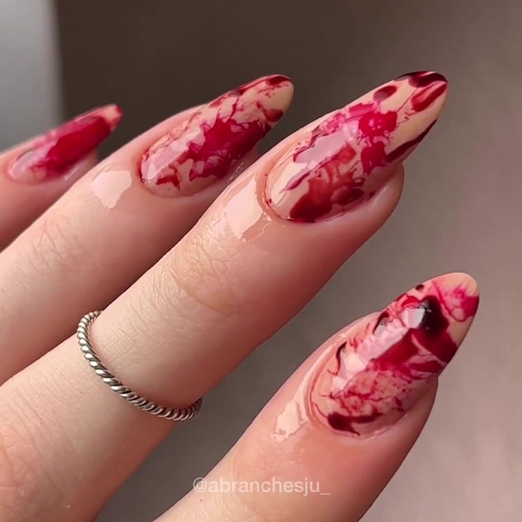 Mão com unhas amendoadas longas decoradas com efeito de sangue espirrado para o Dia das Bruxas