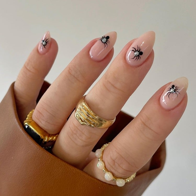 Mão com unhas amendoadas médias nude decoradas para o Halloween com aranhas pretase pedrinha prata