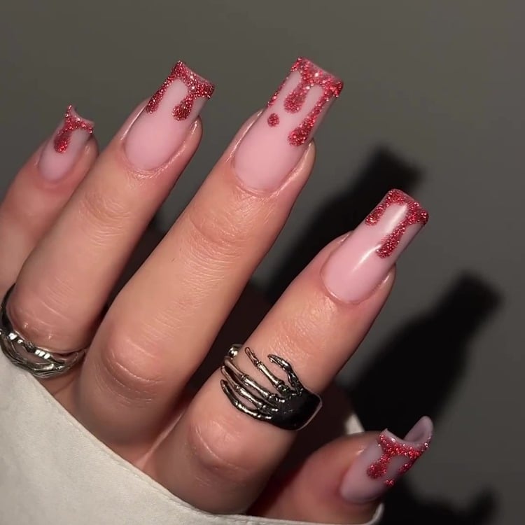 Mão com unhas grandes quadradas decoradas para o Halloween com efeito de sangue pingando, com esmalte de glitter vermelho