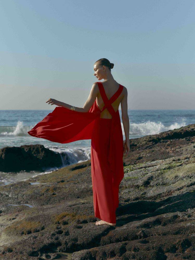 Modelo Yana Trufanova de costas usando um conjunto de blusa trançada nas costas e calça leve, ambas da cor vermelha da coleção Cruise Collection 24 da Lenny Niemeyer. A foto foi tirada na praia do Rio de Janeiro.