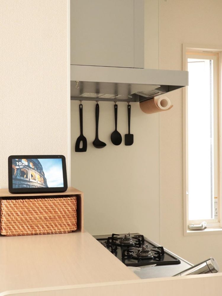 Alexa com visor posta em uma cozinha clean, com coifa, talheres de silicone pretos pendurados e fogão cooktop. 