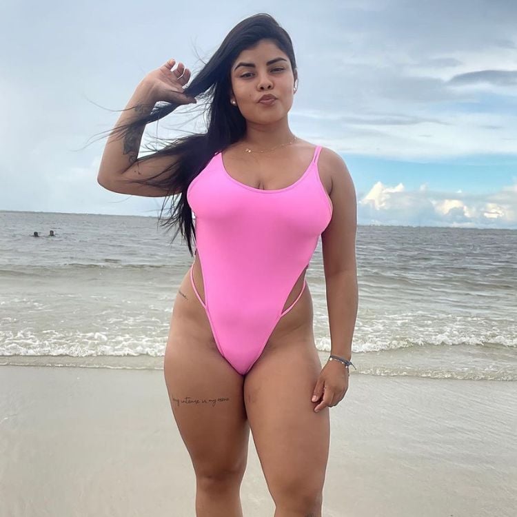 Mulher posa de maiô rosa cavado na praia
