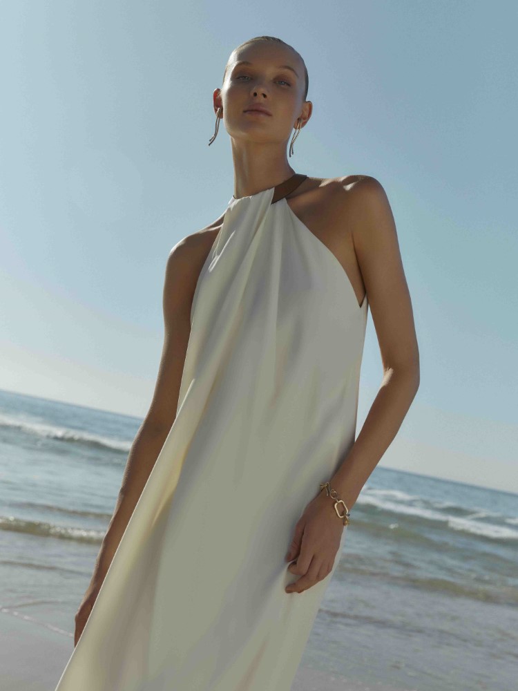Modelo Yana Trufanova usando vestido off white com detalhe no pescoço da coleção Cruise Collection 24 da Lenny Niemeyer. A paisagem é o mar do Rio de Janeiro.