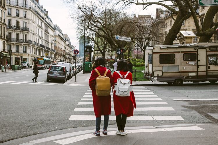 Duas pessoas com casacos vermelhos e mochilas coloridas andando pelas ruas de Paris