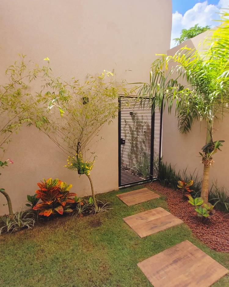Imagem de fachada de casa simples por dentro, com portão de grade preto, gramado, caminho de madeira retangulares grande para andar e plantas no jardim