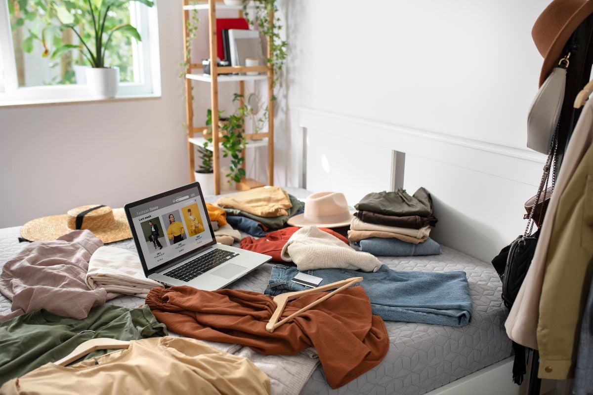foto de quarto decorado com peças espalhadas na cama e notebook mostrando como vender roupas usadas em brechó online