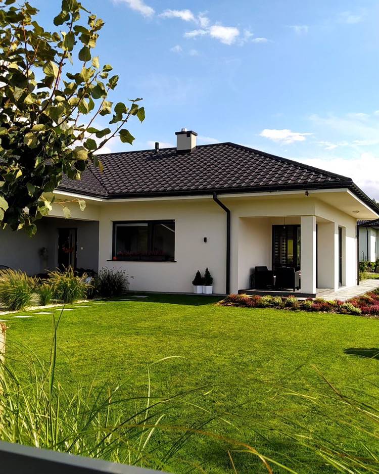 Imagem de fachada de casa simples e chique, com gramado verde e jardim de plantas ao redor