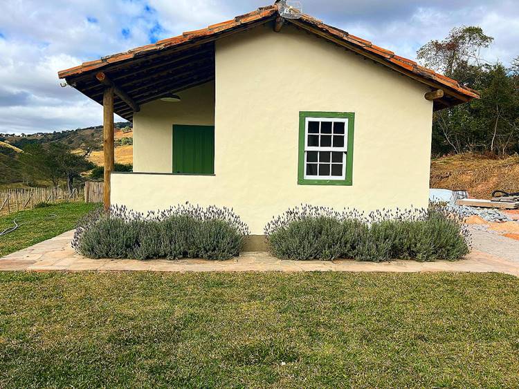 Imagem de fachada de casa simples na Roça. Entrada da casa com porta verde e janela com portal verde possui jardim com lavandas floridas