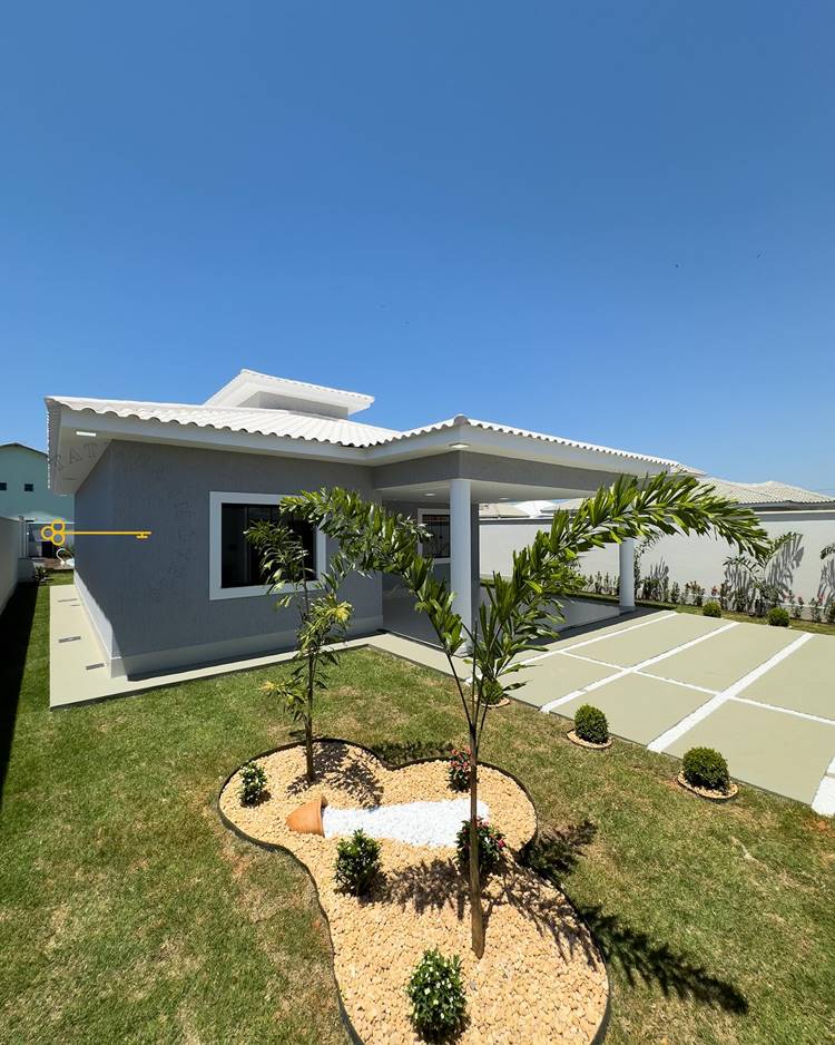 Imagem de fachada de casa simples grande, com jardim gramado, caminho em cimento e pedra para a garagem. Jardim decorado com palmeira e plantinhas
