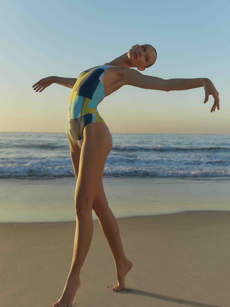 Modelo Yana Trufanova usando um maiô em tons de azul claro e escuro, além de amarelo. A paisagem é a praia carioca. 