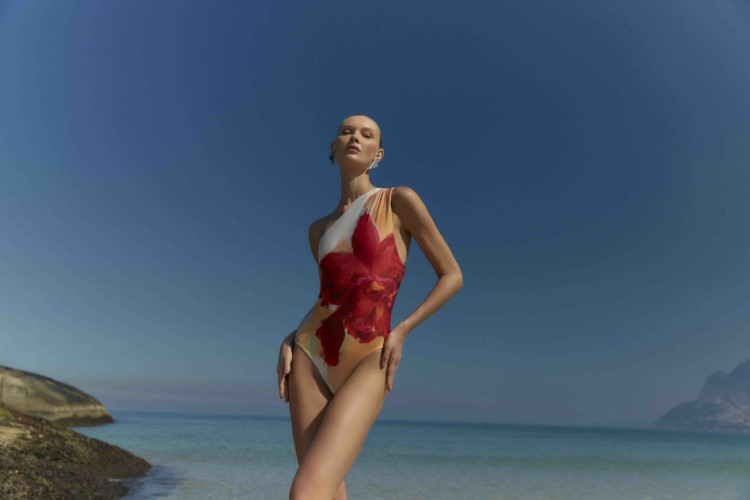Modelo Yana Trufanova posando na praia com um maiôtransversal de flor vermelha da coleção Cruise Collection 24 da Lenny Niemeyer