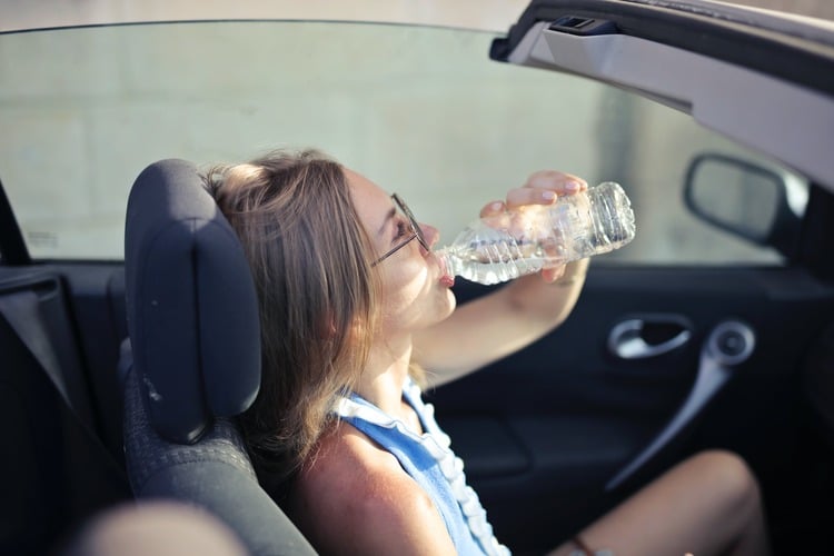 Mulher jovem, branca, em um carro conversível, bebendo água na garrafa