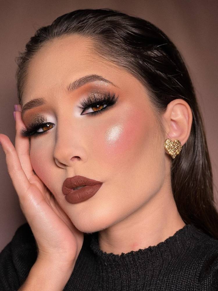 Mulher oriental com maquiagem iluminada nos olhos, blush rosa, bastante iluminador e batom marrom.