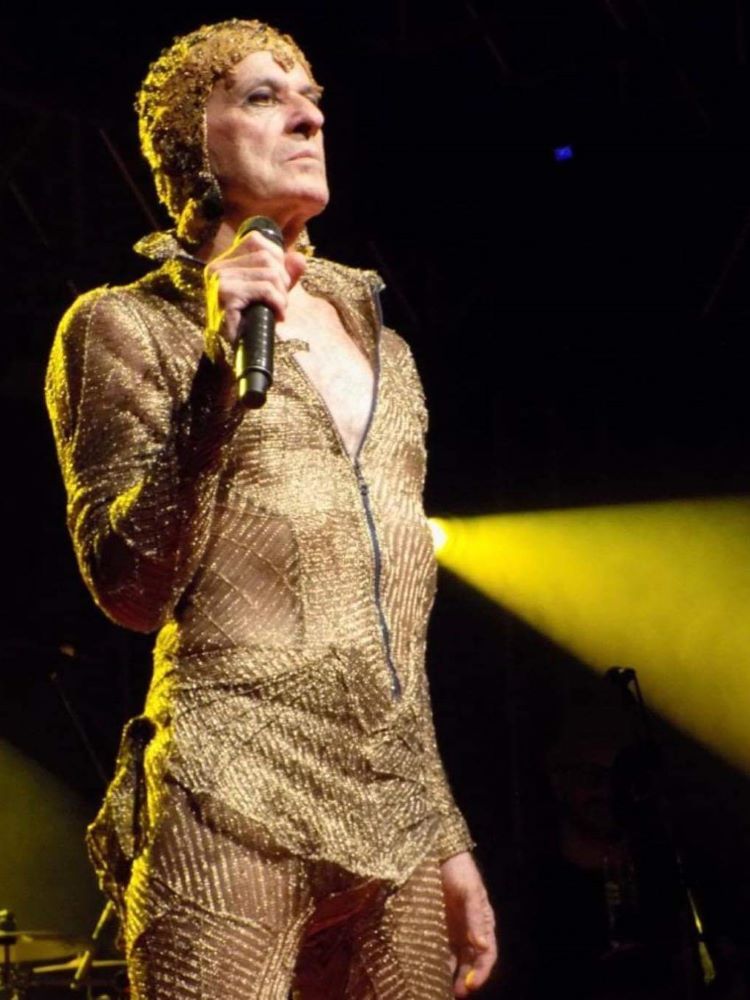 Ney Matogrosso em 2020 usando roupa dourada com transparência e segurando o microfone durante o show.