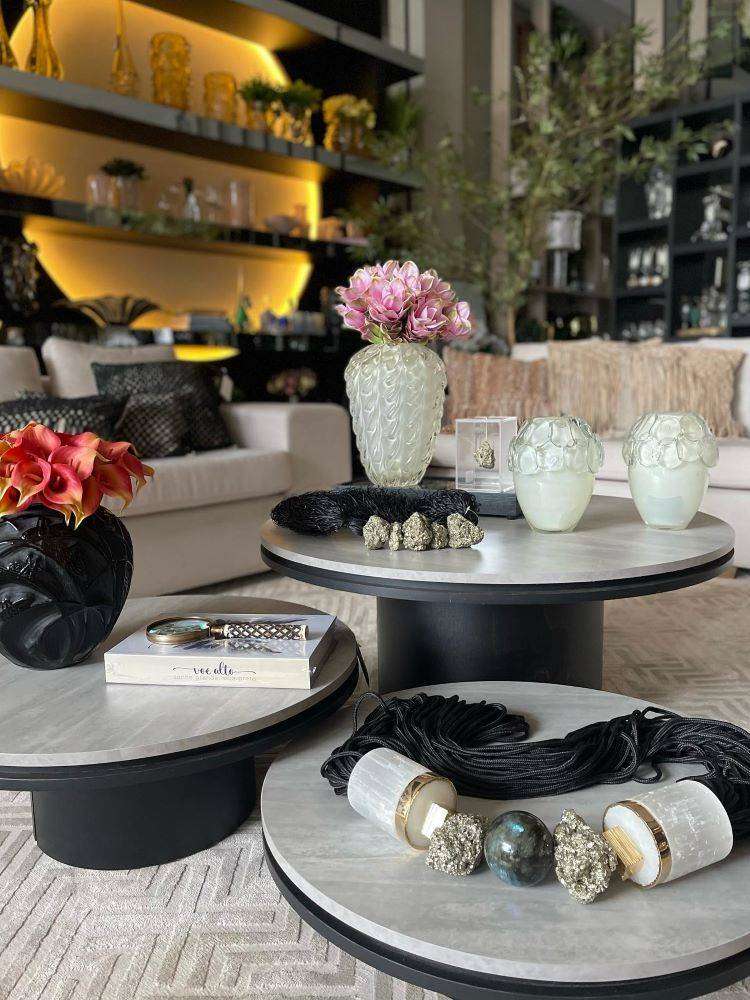 Sala de estar iluminada com mesas de centro com decoração de vasos de vidro em branco e em preto, além de uma corrente decorativa em pedras naturais.