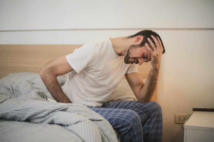 homem sentado na cama com a mãos nas costas, o que ode significar dor nos rins ou infecção renal