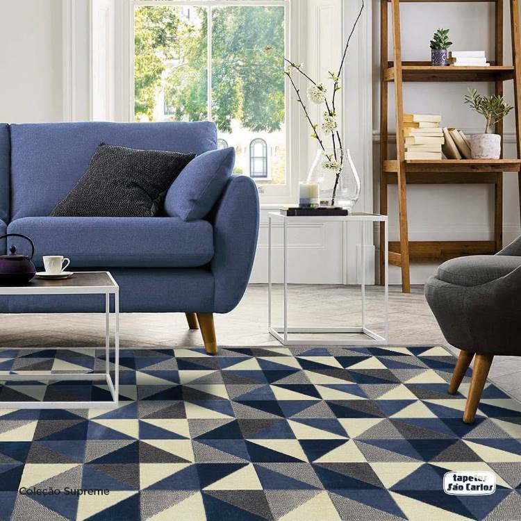 Sala de estar com sofá azul, estante de madeira e tapete geométrico em tons de azul, branco, cinza escuro e cinza claro. 
