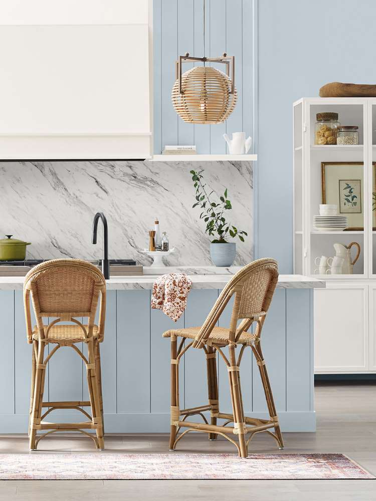 Cozinha em tons de branco e Upward, com cadeiras de madeira, mármore na parede da pia e estante branca com itens de decoração.