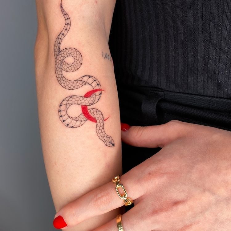 uma tatuagem de cobra em preto com uma lua vermelha próximo ao cotovelo, na parte de dentro do braço