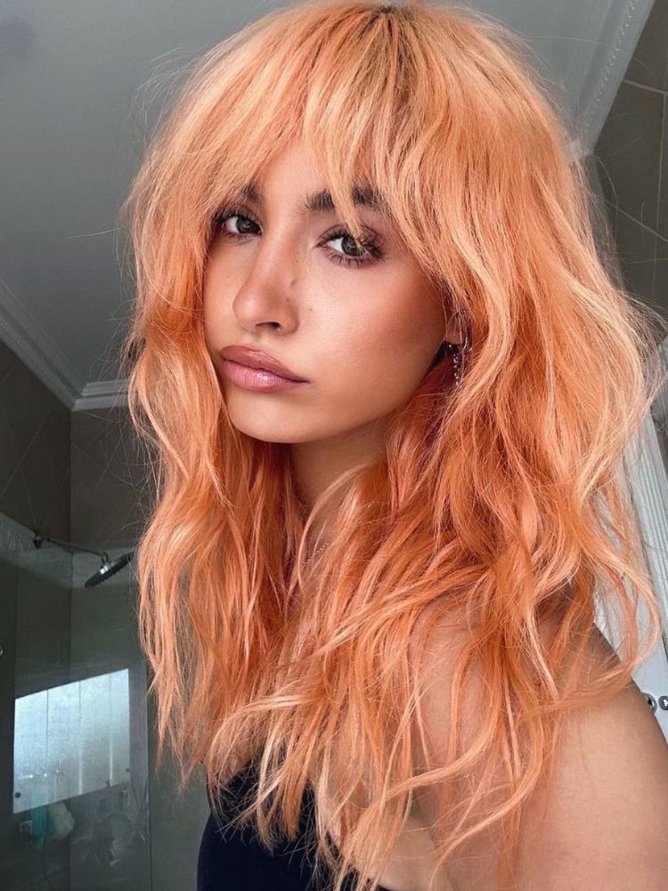 mulher usando cabelo longo com franja e mechas na cor do ano Pantone 2024, Peach Fuzz