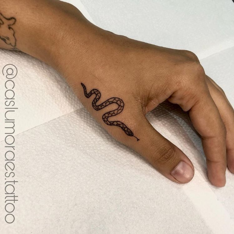 Uma mão com uma tatuagem de cobra próxima ao polegar