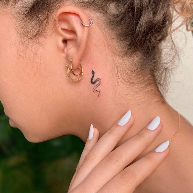 Uma mulher loira de perfil, mostrando uma tatuagem de cobra atrás da orelha 